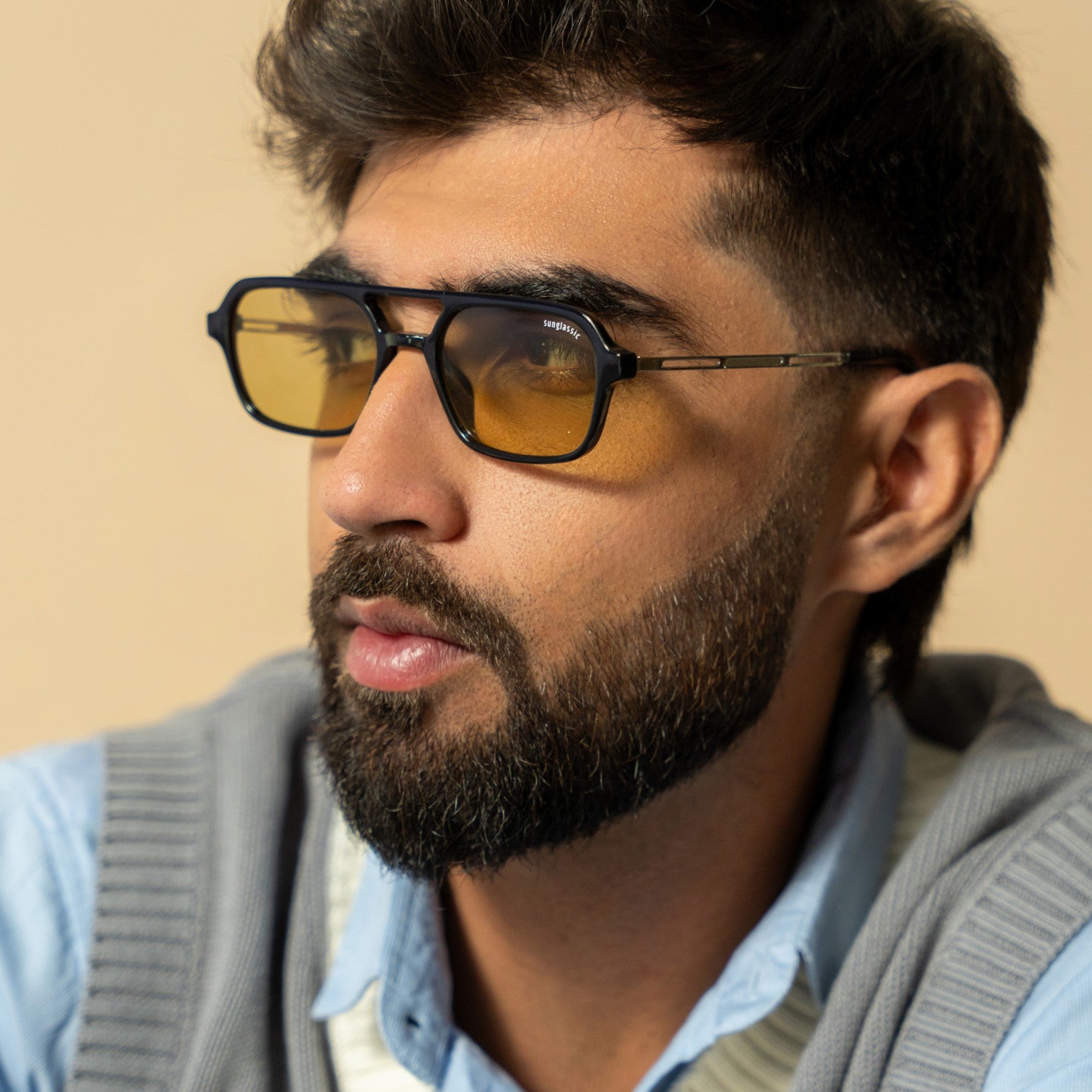Colton Black Green Rectangle Sunglasses – Sunglassic.com. Male model wearing bold black rectangle sunglasses with green-tinted lenses, styled in a blue shirt and grey sweater vest, posed against a soft beige background.
