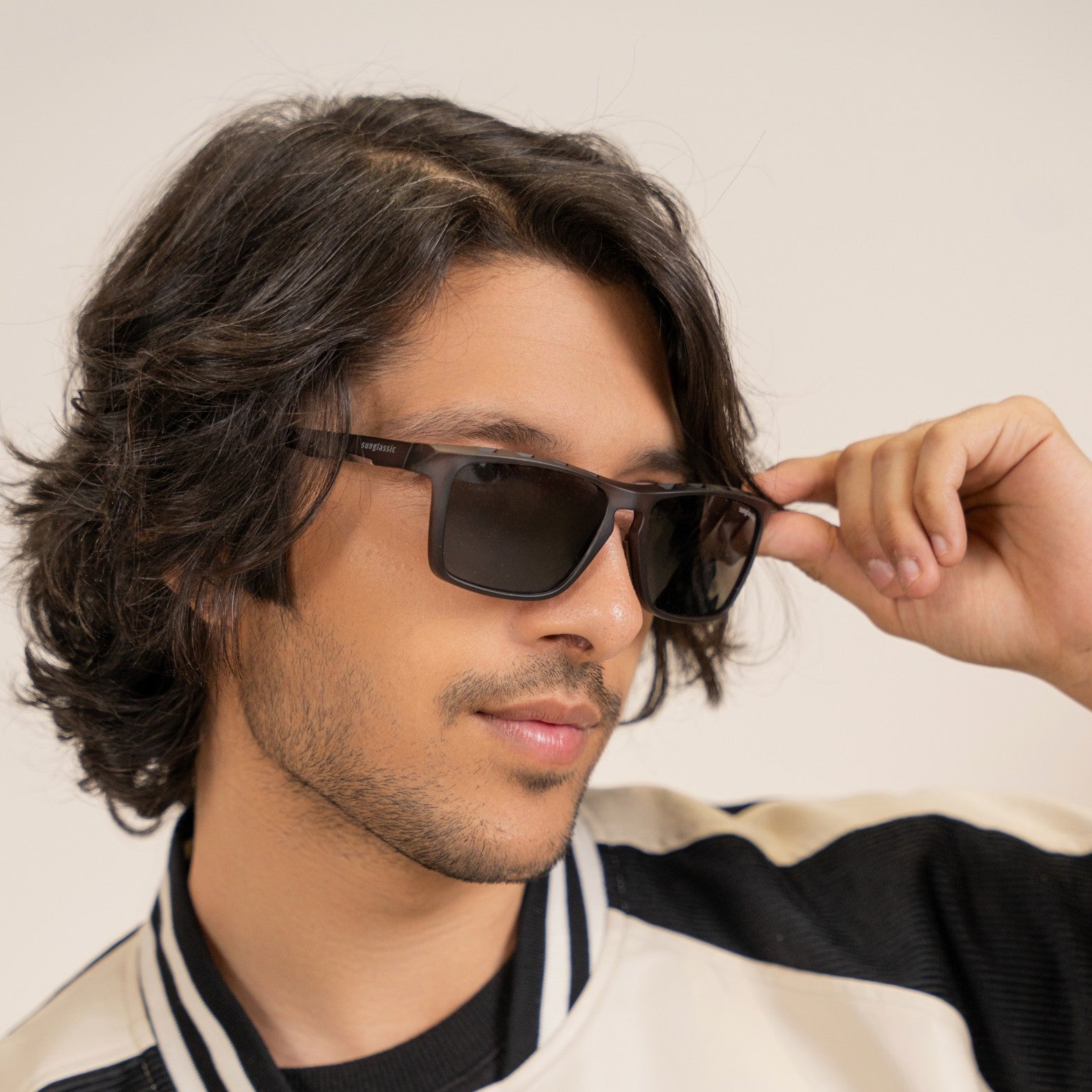 Hawk Grey Black Polarized Rectangle TR90 Sunglasses – Sunglassic.com. Male model wearing sleek polarized rectangle sunglasses with black lenses and grey TR90 frames, styled in a sporty varsity jacket, posing confidently against a neutral background.