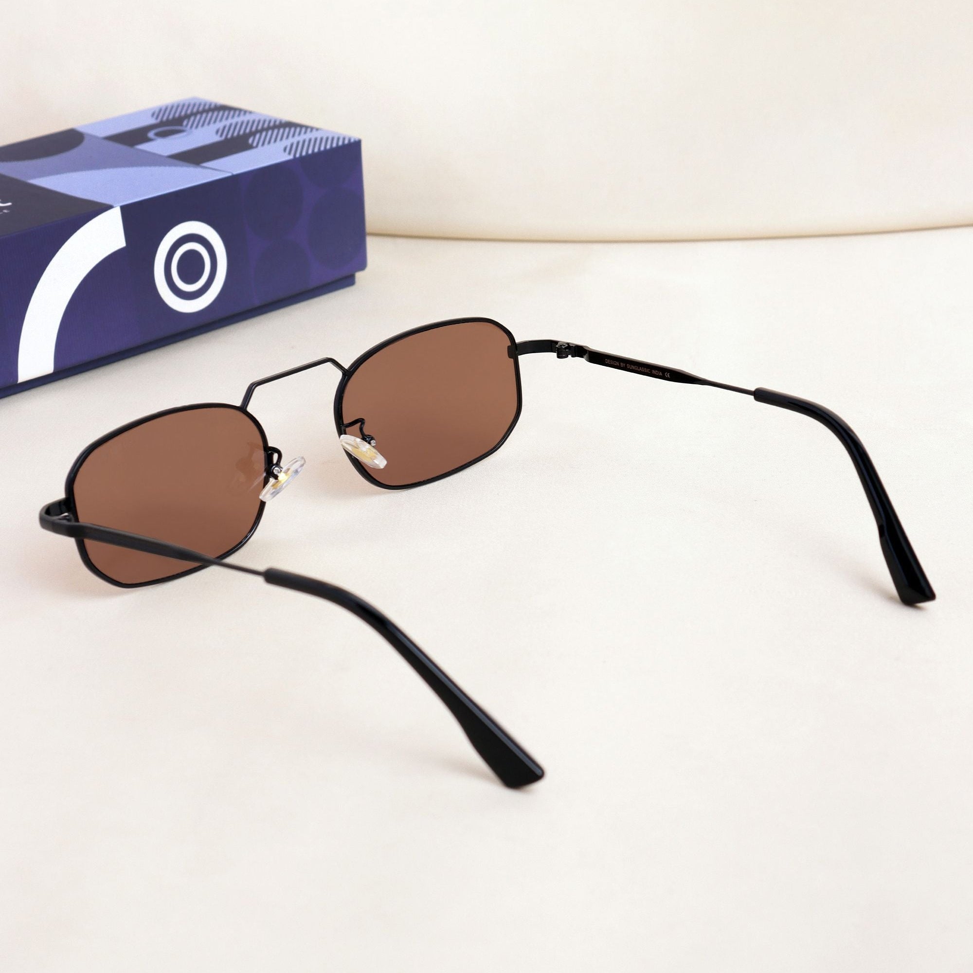 Sunglasses with black frames and brown lenses on a white background, with a blue box featuring a white logo in the background.