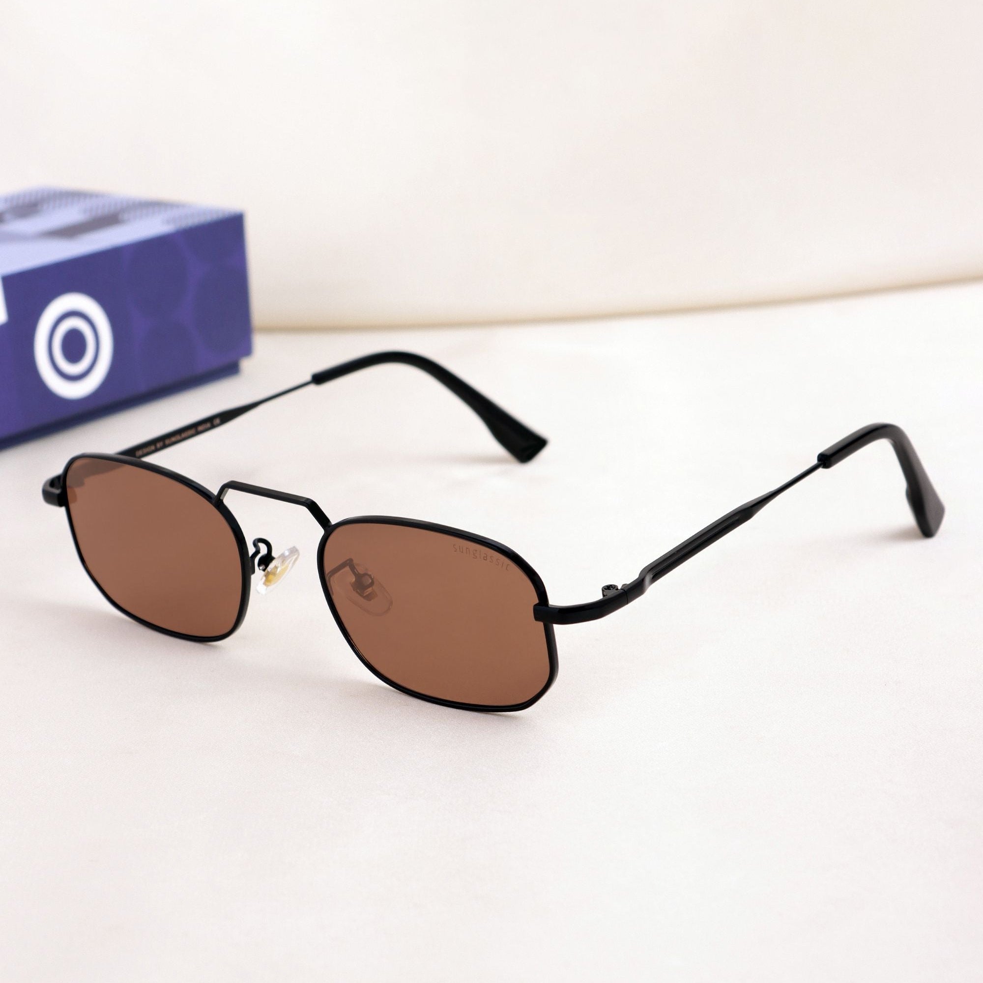 Small oval sunglasses with brown lenses on a white surface, with a blue box in the background.