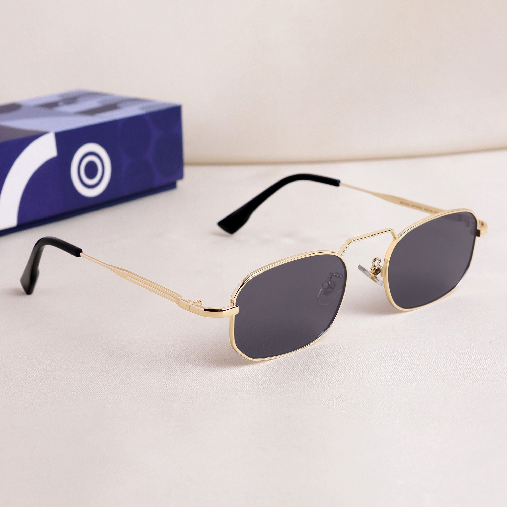 Gold-framed sunglasses with black lenses on a white surface, with a blue box in the background.